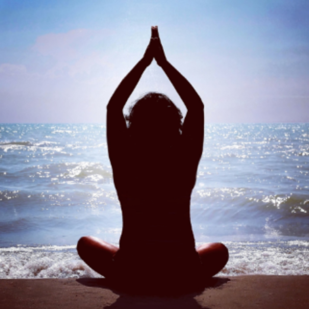 Sitting on the beach in Lotus Position arms raised up in Anjali Mudra/Prayer Position